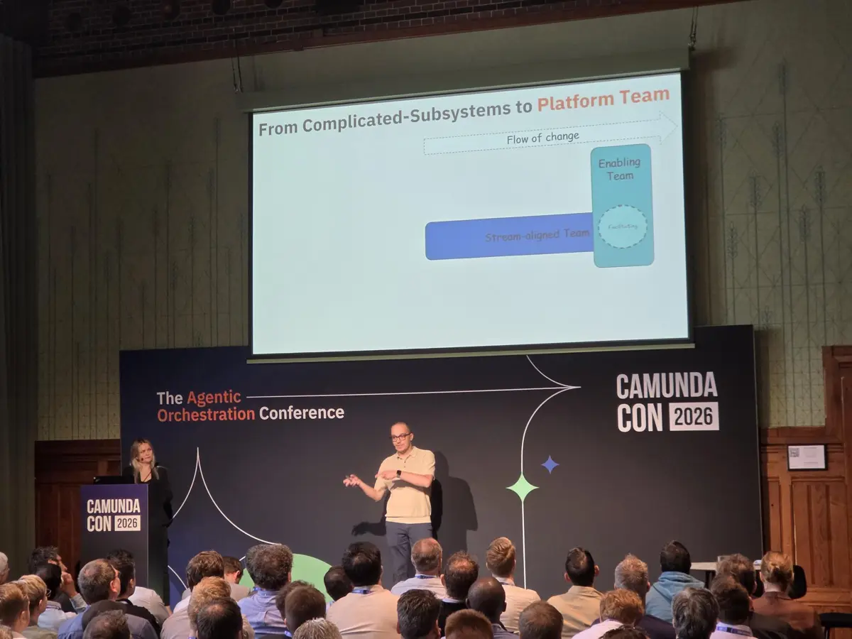 Maria Alish und Thomas Heinrichs auf der Bühne der CamundaCon 2026 vor der Slide "From Complicated-Subsystems to Platform Team".